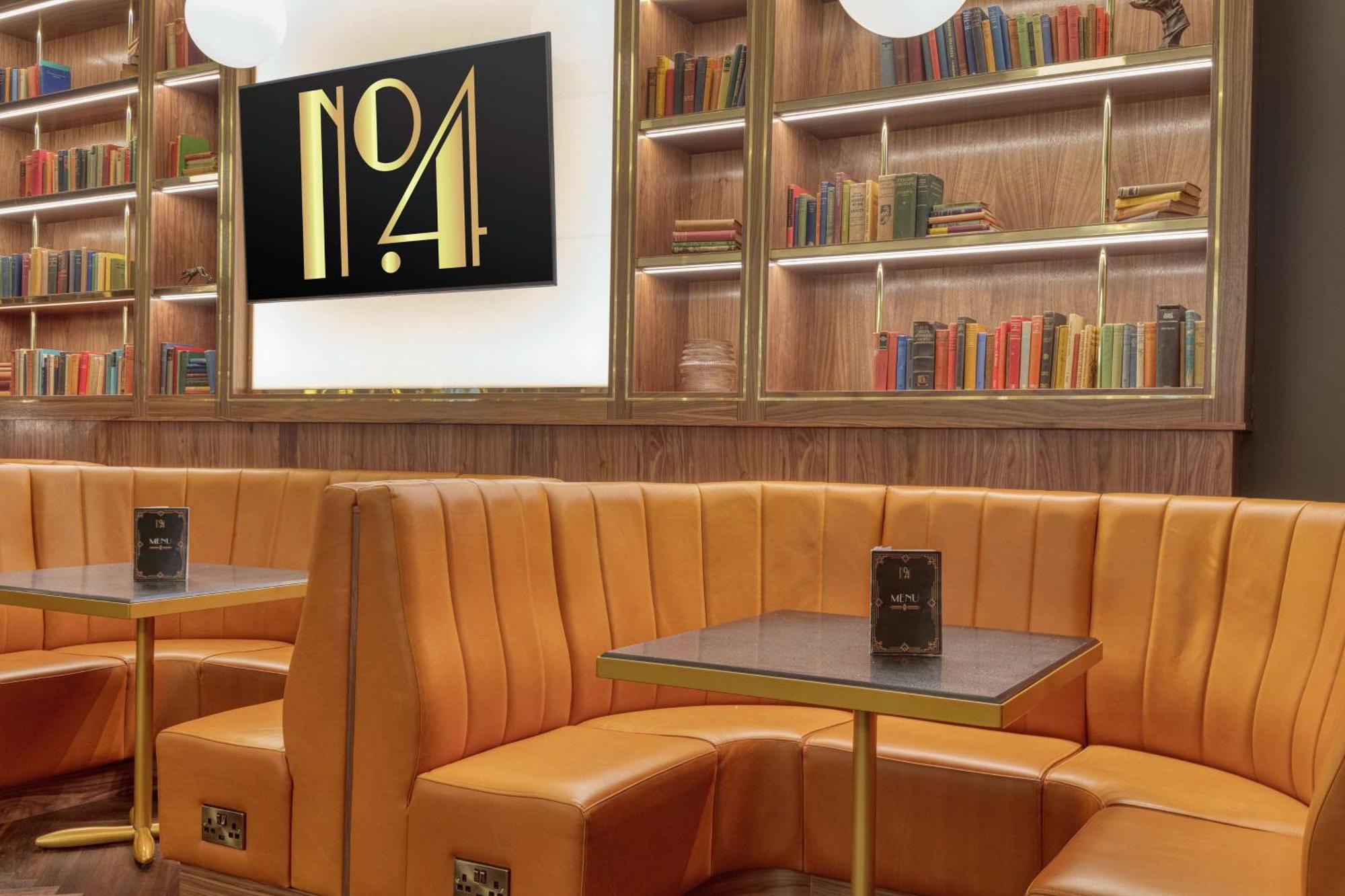 Hilton Belfast Ξενοδοχείο Εξωτερικό φωτογραφία The photo shows a cozy interior space featuring a stylish seating area. There are plush, orange leather booths with an elegant design, arranged around small tables. The background includes a wooden bookshelf filled with a variety of colorful books. A