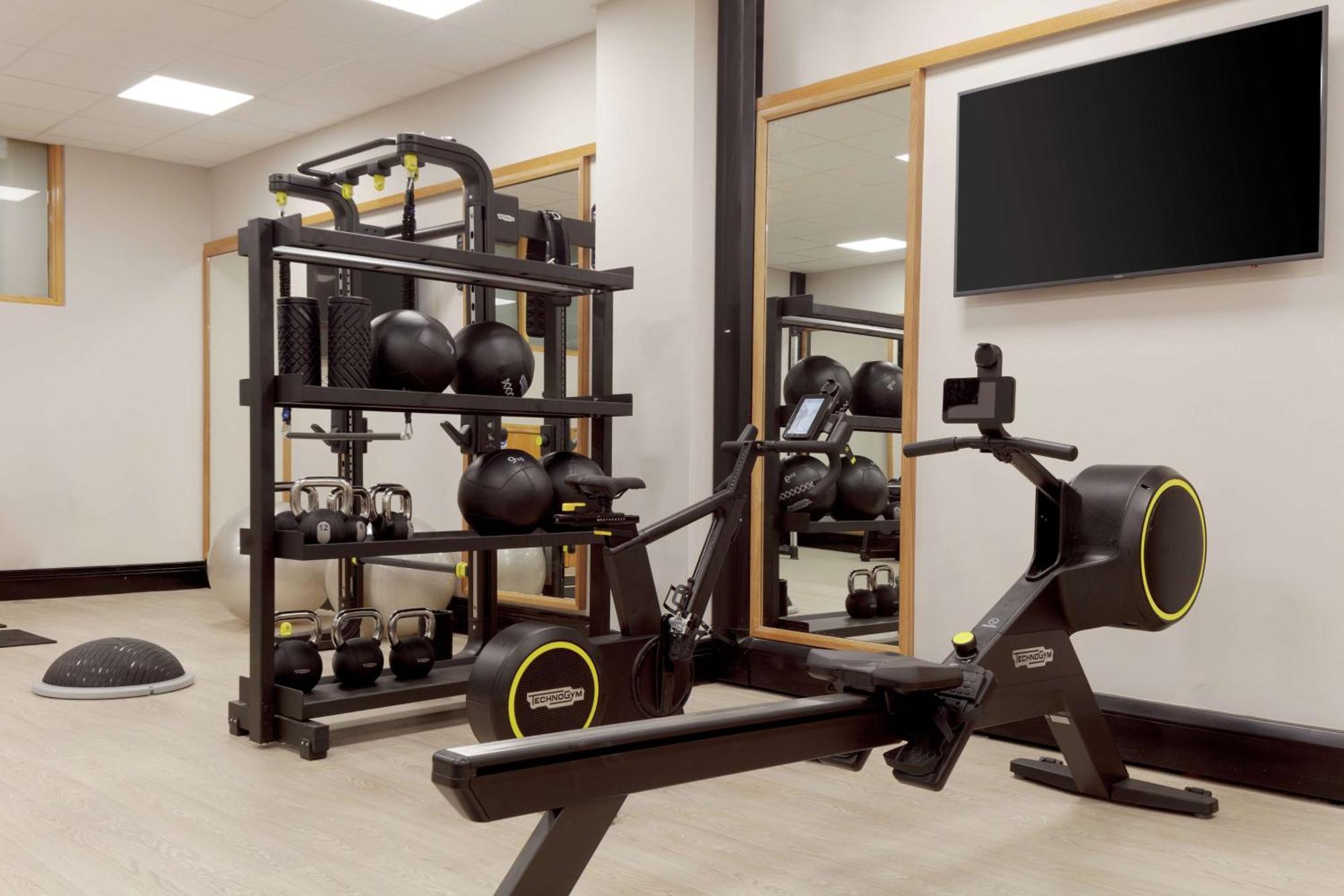 Hilton Belfast Ξενοδοχείο Εξωτερικό φωτογραφία The photo shows a fitness area featuring various exercise equipment. On the left side, there is a rack that holds multiple black kettlebells and a few other fitness accessories. In the center, there is a rowing machine designed for cardio workouts. T