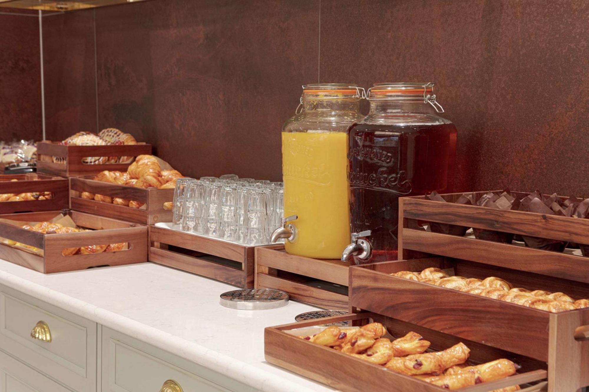 Hilton Belfast Ξενοδοχείο Εξωτερικό φωτογραφία The photo shows a buffet-style setup featuring various food and beverage items. There are several wooden trays filled with pastries, including croissants and other baked goods. In the background, there are two large glass jars, one filled with yellow